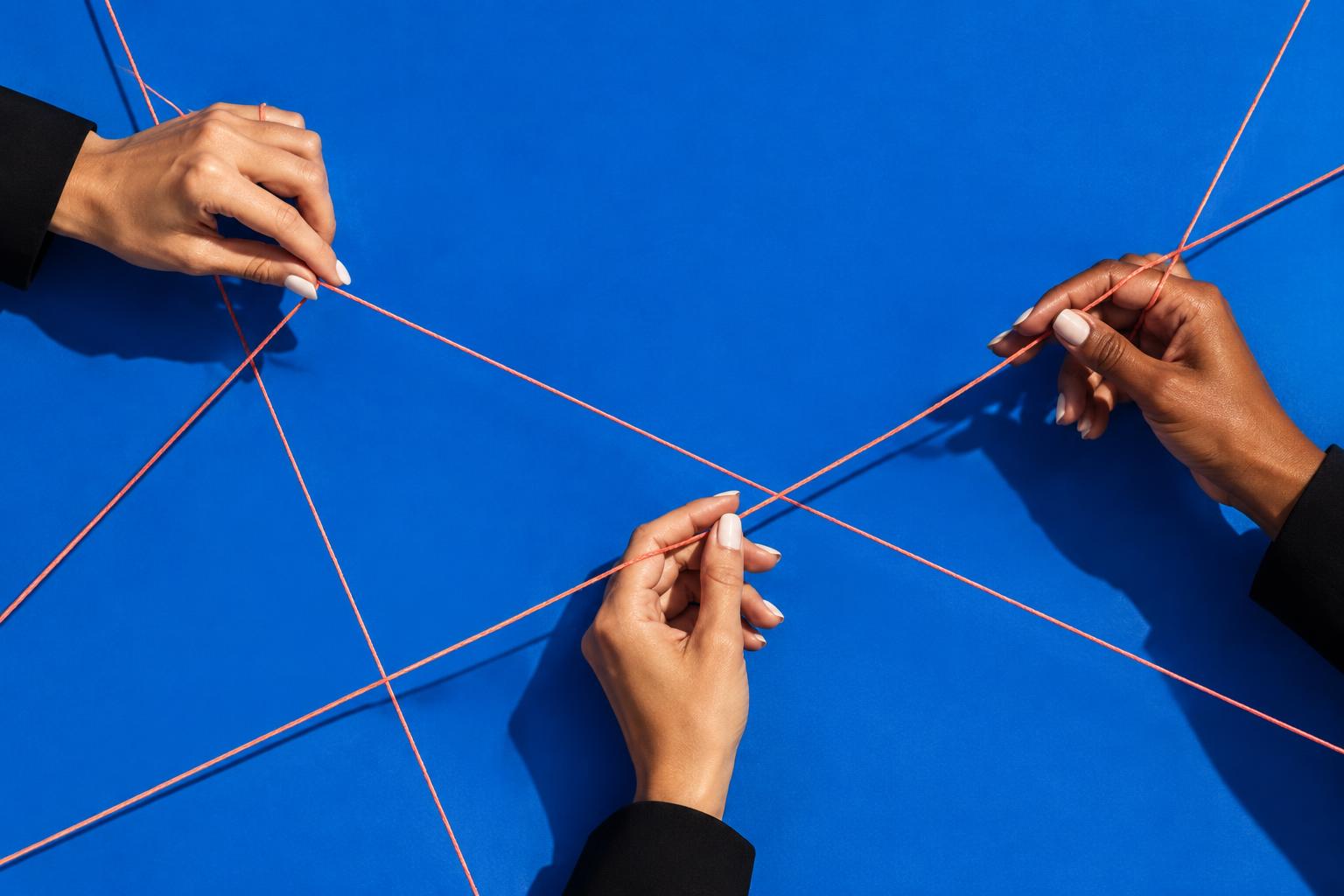 Manos que unen hilos coral sobre un fondo azul